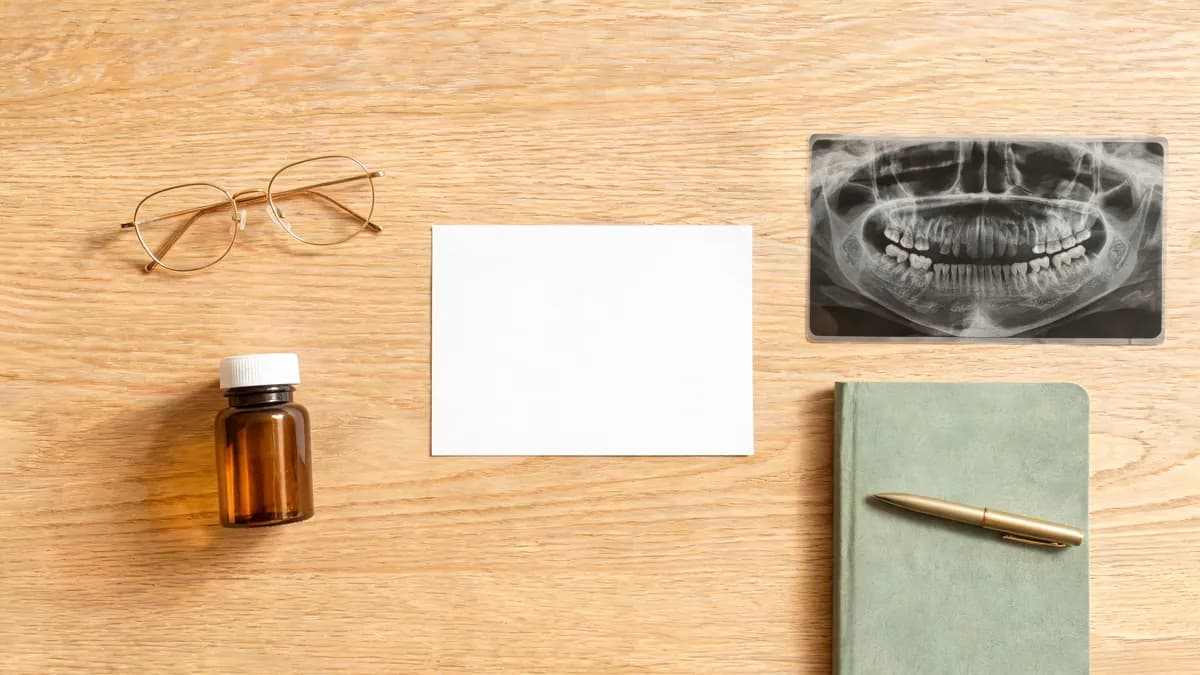 Items to bring to a first oral surgery visit laid out on a desk: a card, a pill bottle, a dental X-ray, a notebook and glasses