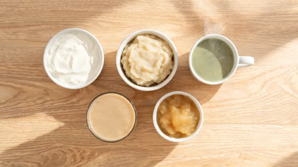 Soft foods for wisdom teeth recovery on a table: yogurt, mashed potatoes, blended soup, applesauce and a smoothie in a glass